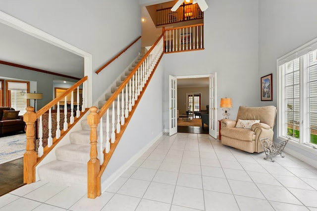 stairway with a towering ceiling, baseboards, french doors, ceiling fan, and tile patterned floors