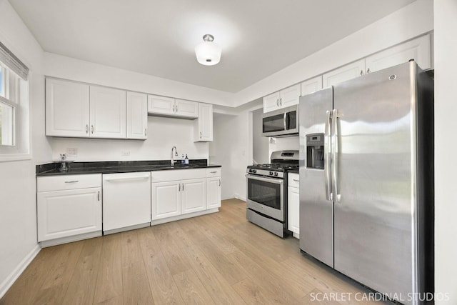 kitchen with stainless steel appliances, a sink, white cabinetry, dark countertops, and light wood-style flooring