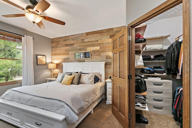 bedroom featuring a ceiling fan, dark carpet, wooden walls, and an accent wall