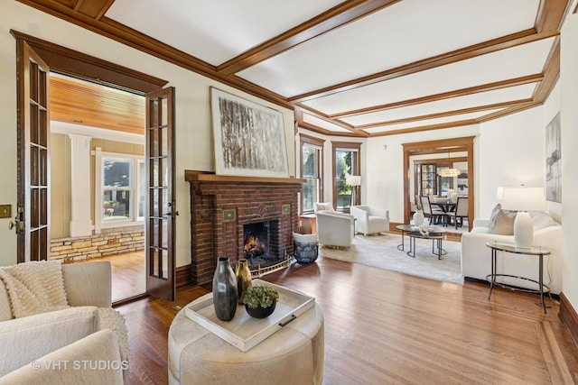 living area featuring wood finished floors, a brick fireplace, baseboards, beam ceiling, and crown molding
