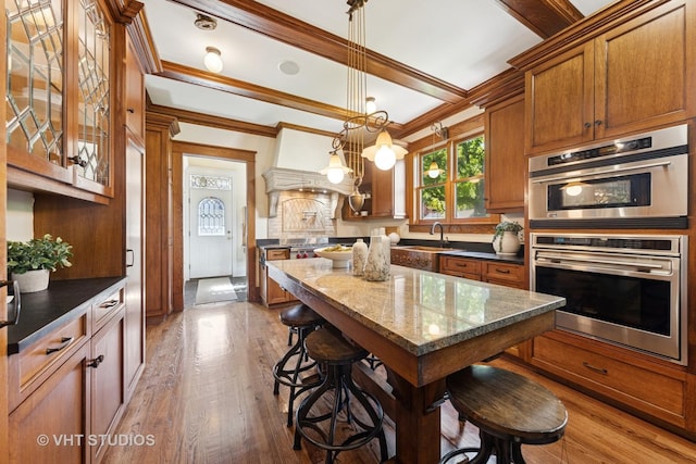 kitchen with crown molding, stainless steel double oven, a sink, brown cabinets, and wood finished floors