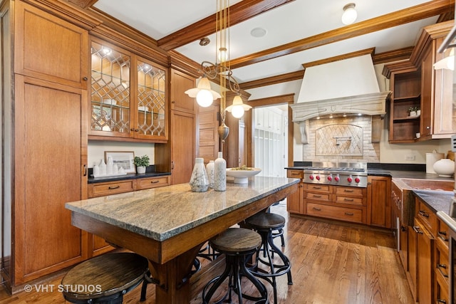 kitchen featuring premium range hood, brown cabinets, wood finished floors, ornamental molding, and beamed ceiling