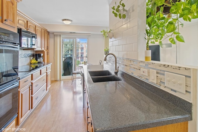 kitchen featuring a sink, black appliances, light wood finished floors, decorative backsplash, and dark countertops