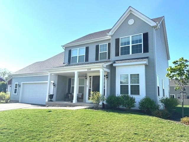 traditional-style home featuring a front lawn, concrete driveway, covered porch, and an attached garage