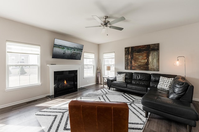 living room with ceiling fan, baseboards, a glass covered fireplace, and wood finished floors