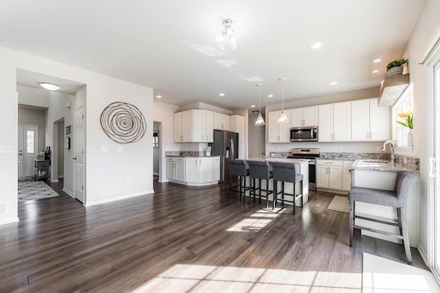 kitchen featuring stainless steel appliances, a breakfast bar area, white cabinets, light stone countertops, and a kitchen island