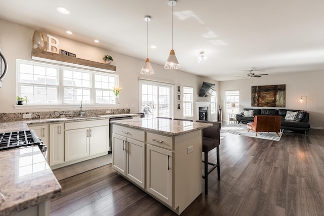 kitchen with a sink, a fireplace, ceiling fan, a kitchen bar, and a kitchen island