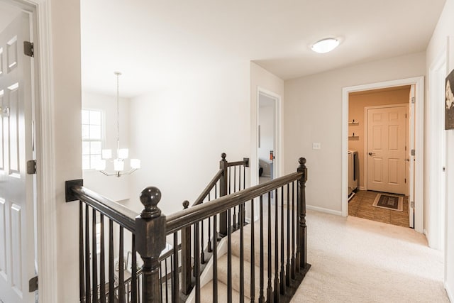 hall with an inviting chandelier, carpet floors, baseboards, and an upstairs landing