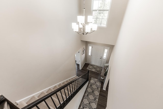 stairs featuring a chandelier, wood finished floors, baseboards, and a high ceiling