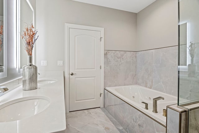 bathroom with double vanity, a tub with jets, marble finish floor, and a sink