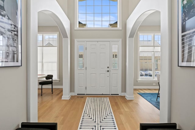 entryway featuring light wood-style floors, baseboards, arched walkways, and a healthy amount of sunlight