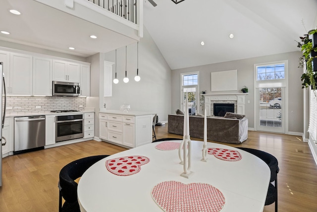 kitchen featuring light wood finished floors, white cabinetry, high vaulted ceiling, a fireplace, and appliances with stainless steel finishes