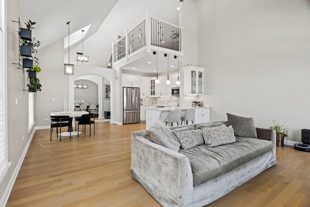 living area with light wood-style flooring, baseboards, arched walkways, and high vaulted ceiling