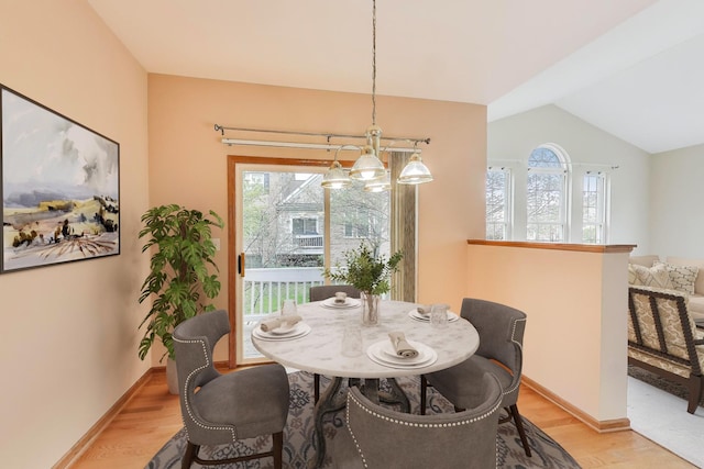 dining space featuring plenty of natural light, light wood-style floors, vaulted ceiling, and baseboards