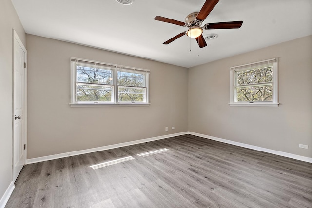 spare room featuring a wealth of natural light, baseboards, wood finished floors, and a ceiling fan