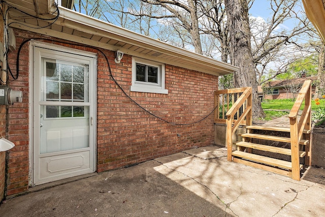 view of exterior entry featuring brick siding, a wooden deck, and a patio area