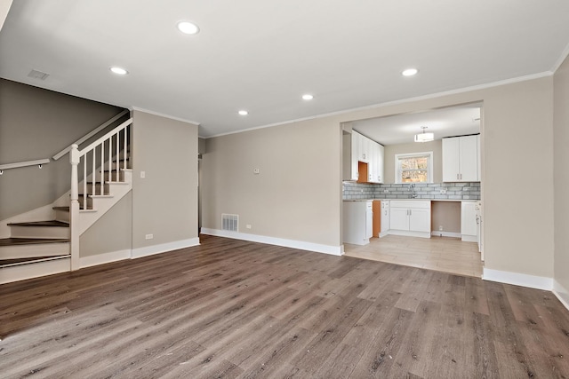 unfurnished living room featuring light wood finished floors, a sink, visible vents, stairway, and ornamental molding