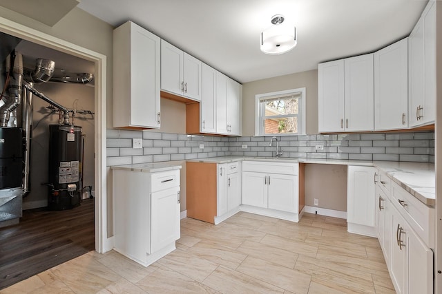 kitchen with light stone countertops, a sink, gas water heater, white cabinetry, and tasteful backsplash