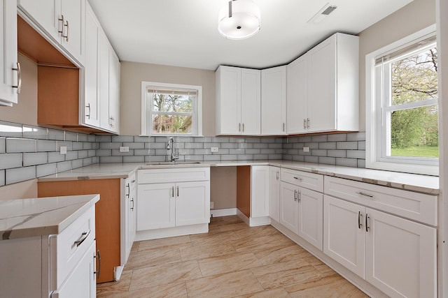 kitchen featuring a sink, white cabinets, visible vents, backsplash, and light stone counters