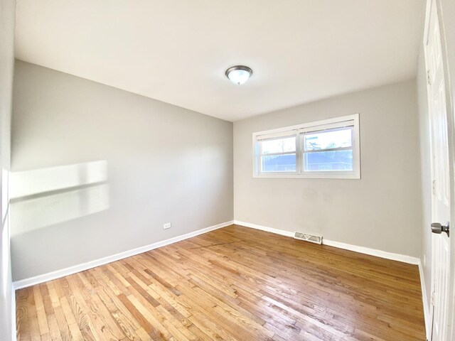 empty room with light wood finished floors, baseboards, and visible vents