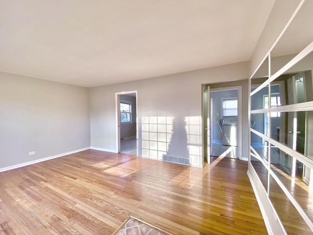 spare room with washer / dryer, visible vents, baseboards, and hardwood / wood-style floors