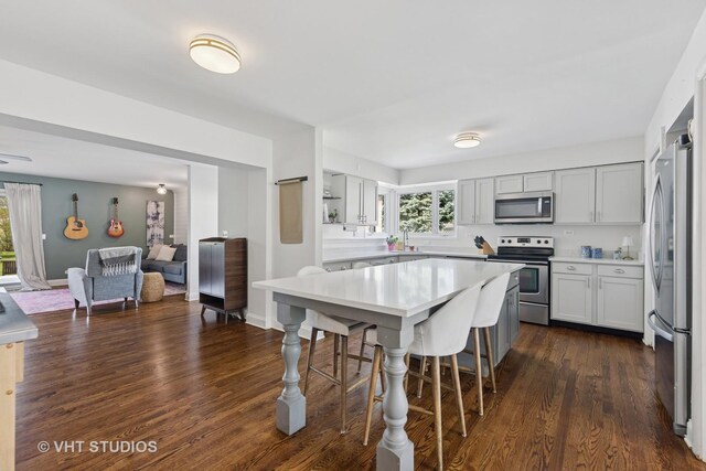 kitchen with stainless steel appliances, a breakfast bar area, light countertops, and dark wood-style floors