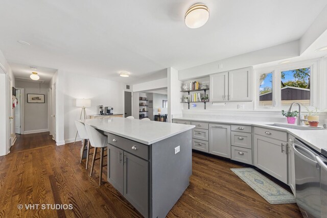 kitchen featuring dishwasher, gray cabinetry, a sink, a center island, and light countertops