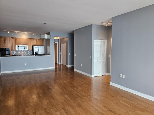 unfurnished living room featuring baseboards, track lighting, and wood finished floors