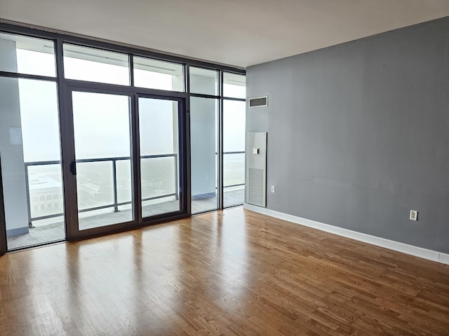 empty room with a wealth of natural light, a wall of windows, visible vents, and wood finished floors