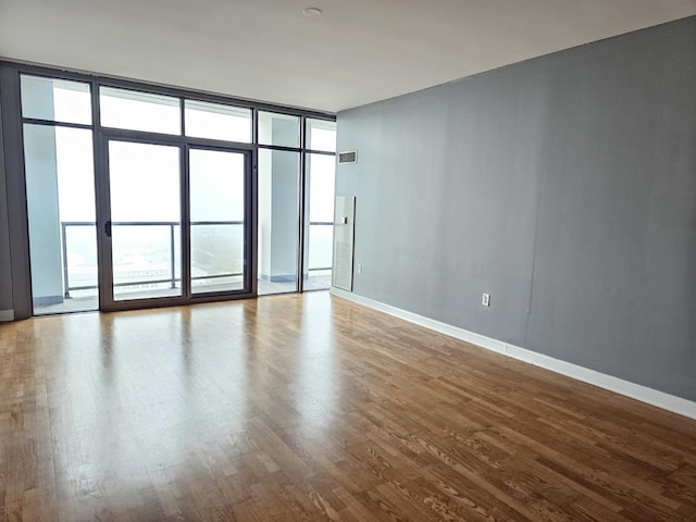 unfurnished room with a wall of windows, baseboards, visible vents, and wood finished floors