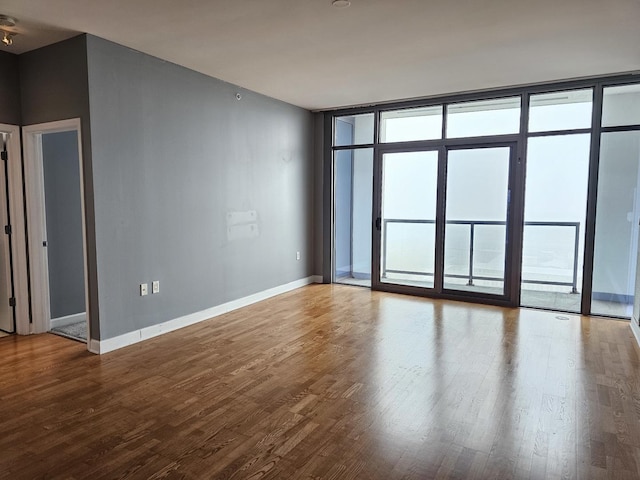 unfurnished room with baseboards, floor to ceiling windows, and wood finished floors