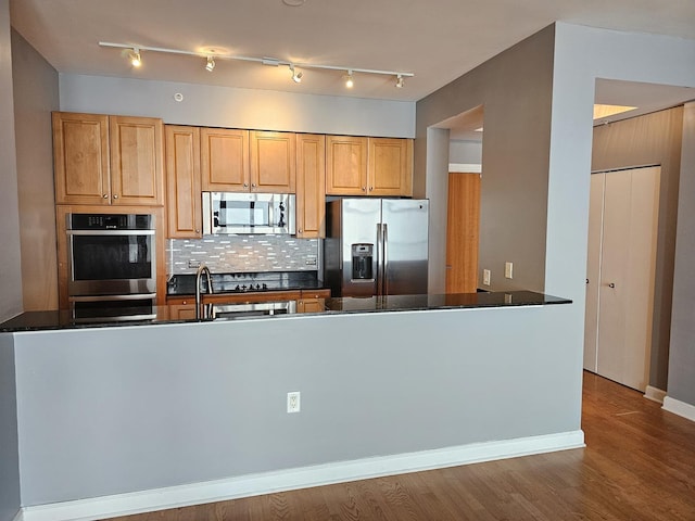 kitchen with a peninsula, wood finished floors, baseboards, appliances with stainless steel finishes, and tasteful backsplash