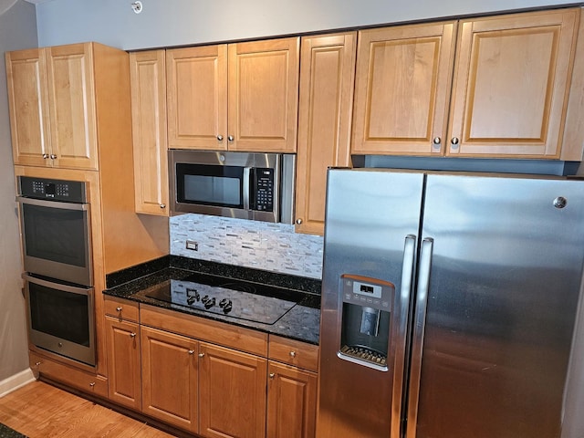 kitchen featuring light brown cabinets, baseboards, light wood-style floors, stainless steel appliances, and dark stone counters