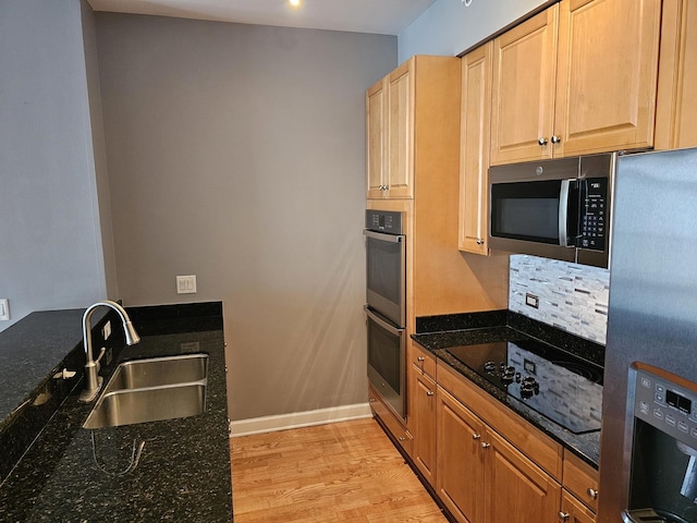 kitchen with light wood-style flooring, baseboards, a sink, dark stone counters, and appliances with stainless steel finishes