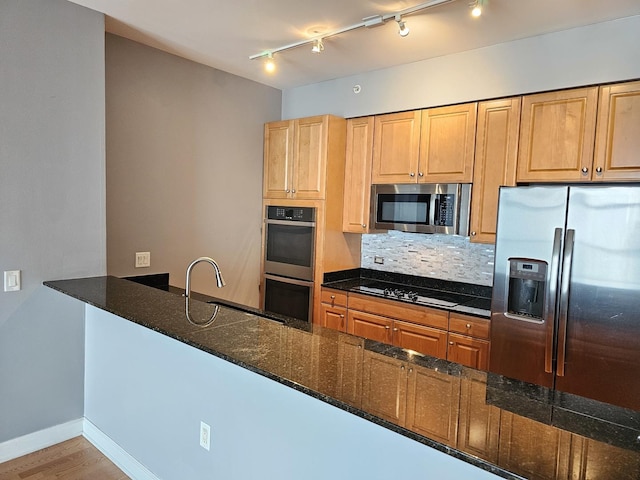 kitchen with dark stone counters, appliances with stainless steel finishes, a sink, and backsplash