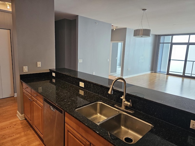 kitchen featuring stainless steel dishwasher, light wood finished floors, a sink, dark stone countertops, and brown cabinets