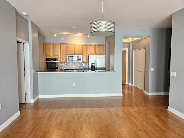 kitchen featuring wood finished floors, decorative backsplash, baseboards, dark countertops, and appliances with stainless steel finishes