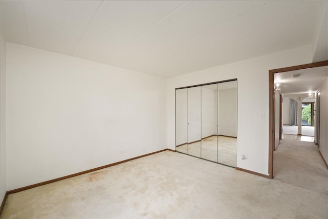 unfurnished bedroom with light carpet, baseboards, a closet, and arched walkways