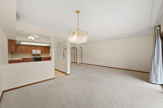 unfurnished living room with light colored carpet, arched walkways, a chandelier, and baseboards