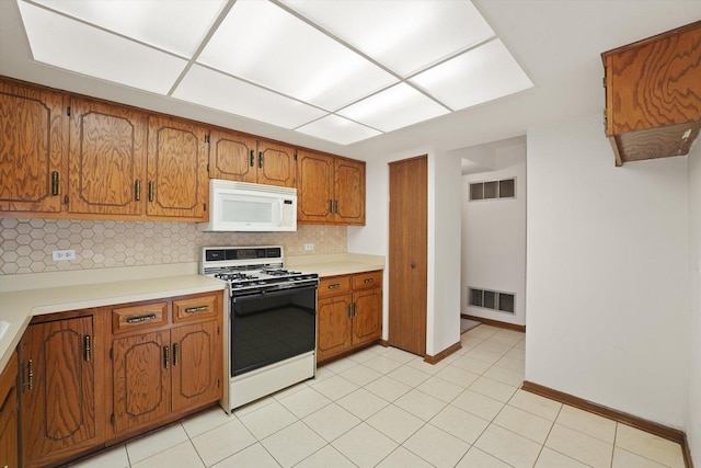 kitchen with white microwave, range with gas stovetop, brown cabinets, backsplash, and light countertops