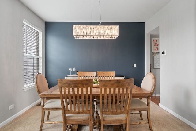 dining space featuring light colored carpet, baseboards, and a notable chandelier