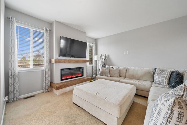 carpeted living area with baseboards, a glass covered fireplace, and visible vents