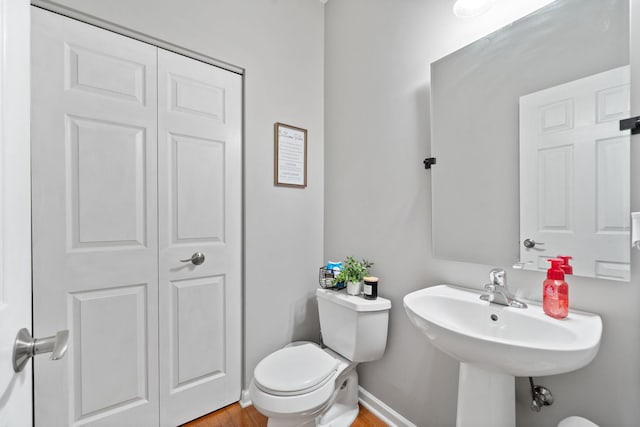 half bath with toilet, baseboards, and wood finished floors