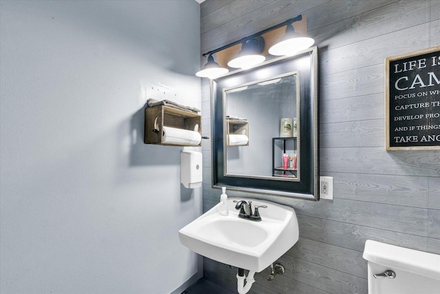 half bath featuring toilet, wood walls, and a sink