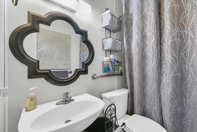 bathroom with toilet, curtained shower, and a sink