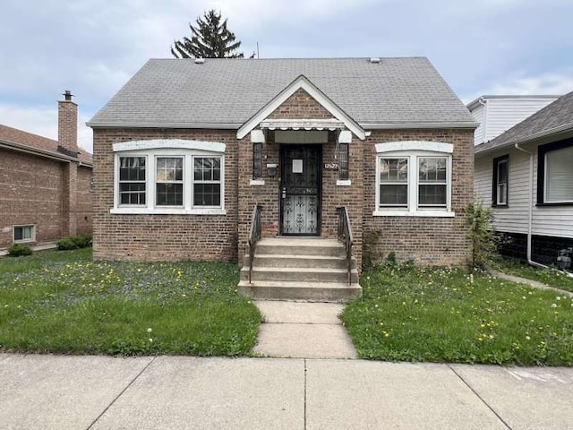 bungalow with brick siding, a front yard, and a shingled roof