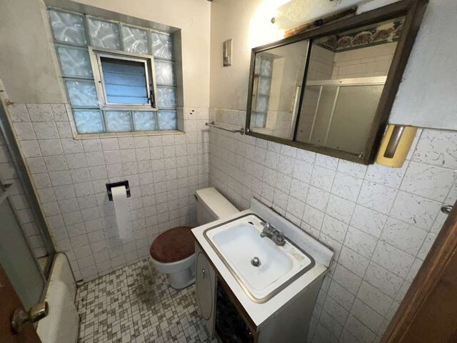 full bathroom featuring tile walls, toilet, a shower with shower door, vanity, and a wainscoted wall