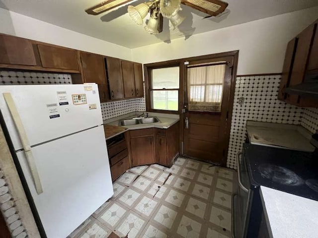kitchen featuring freestanding refrigerator, a sink, a ceiling fan, light flooring, and range with electric stovetop