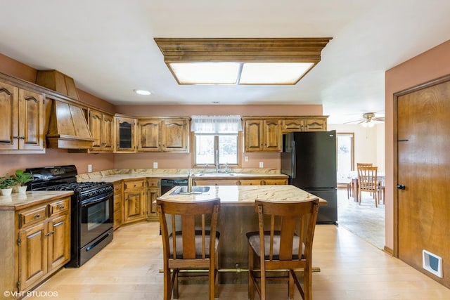 kitchen featuring black appliances, light countertops, premium range hood, brown cabinetry, and light wood finished floors