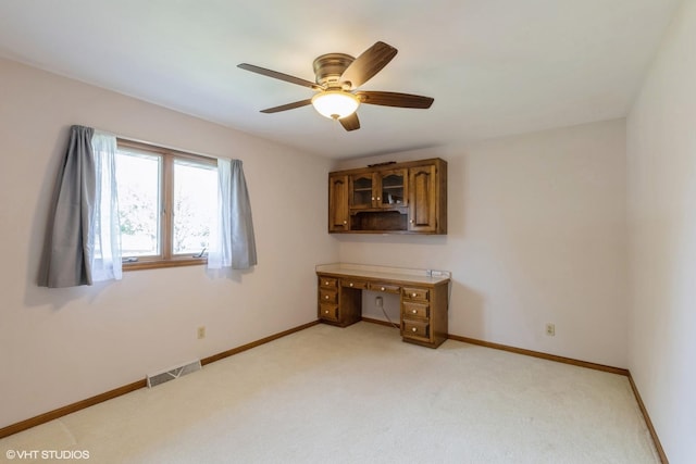 unfurnished bedroom featuring light colored carpet, a desk, baseboards, and a ceiling fan
